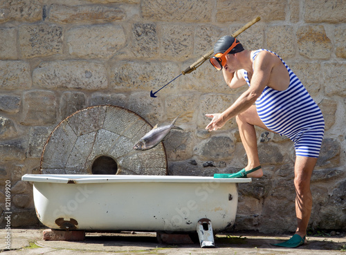 Photography funny man with a harpoon throwing fish in the tub