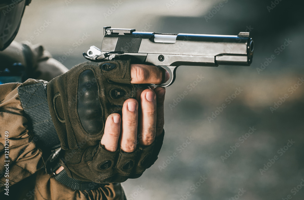 the soldier in the performance of tasks in camouflage and protective gloves holding a pistol with the hammer cocked takes aim for shot. War Zone.