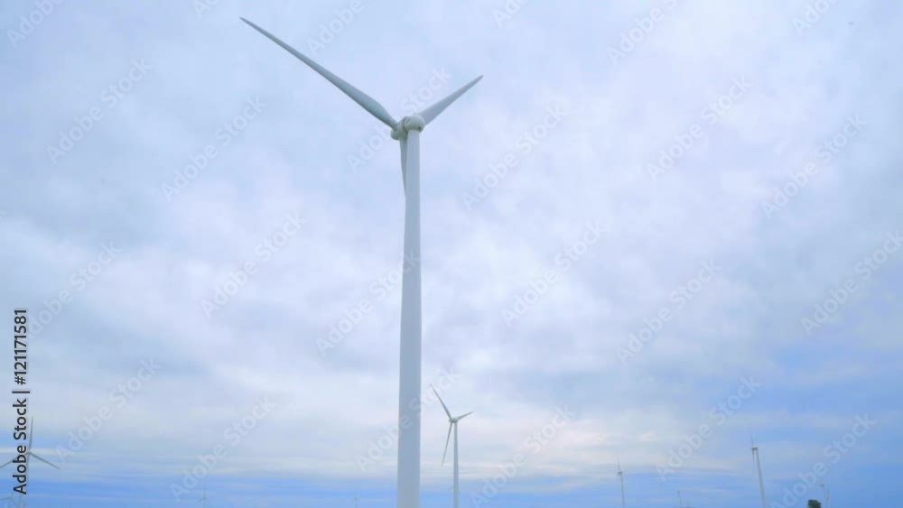 Wind generators. Panning from wind turbines to rural road between two farm fields. Panning on wind turbine on background of cloudy sky. Green field with wind generators. Wind power technology Wind generators. Panning from wind turbines to rural road between two farm fields. Panning on wind turbine on background of cloudy sky. Green field with wind generators. Wind power technology