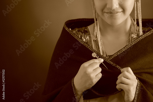 Beautiful hispanic model wearing andean traditional clothing, dark poncho on top, smiling posing for camera while fiddling fingers, studio background, black and white edition photo