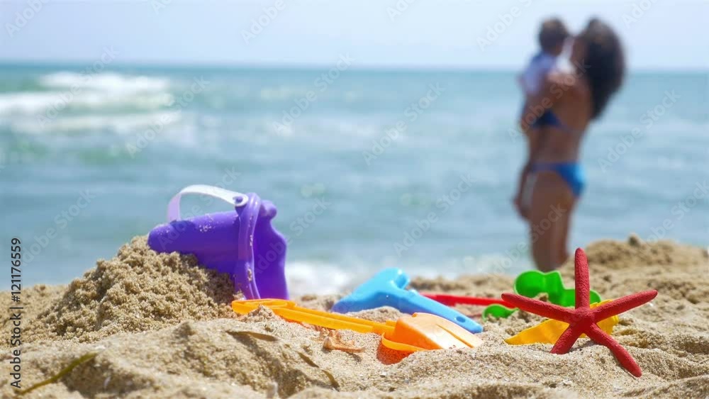 Mother and little son playing at the sea beach, sand toys in front Mother and little son playing at the sea beach, sand toys in front