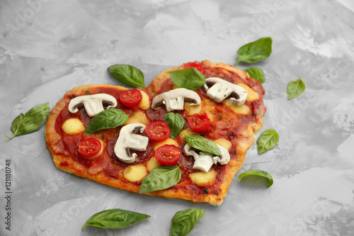 Tasty pizza in heart shape and fresh basil leaves on table