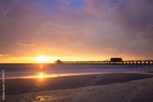 The sun goes down at the Naples Pier in the Gulf of Mexico, Southwest Florida, USA. Amazing landscape spot of the sun coming down at blue hour in this idyllic place for family vacation and relax.