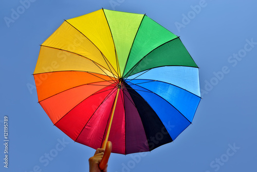 Rainbow umbrella in hand of a man on blue sky