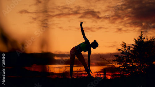 Slender young woman doing fitness exercises in the warm-up at sunset. Flexible shape, smooth motion.
