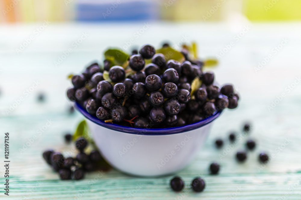 Chokeberry fresh fruits in a bowl on a wooden table in the garden. Chokeberry fresh fruits in a bowl on a wooden table in the garden.