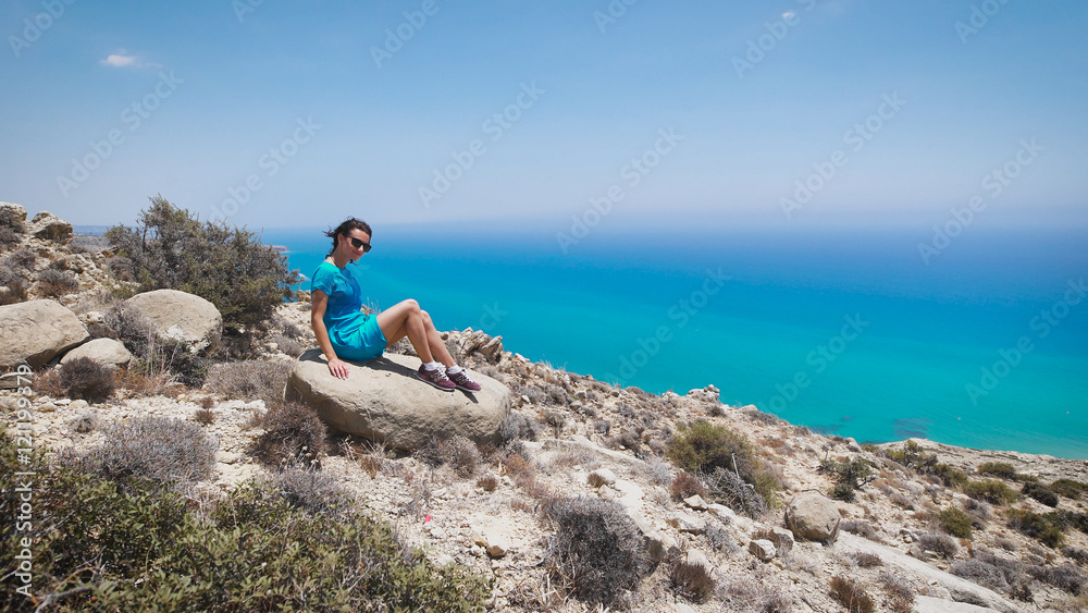A young woman in blue dress sitting on the mountain with the beautiful view to the sea