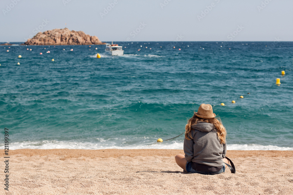 Beach scene. Woman girl traveler sitting on the beach and looking at the sea ocean and waiting for a boat or ferry. Travel concept