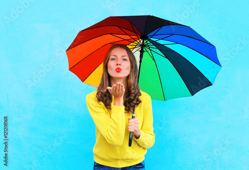 Pretty young woman with colorful umbrella sends air sweet kiss i