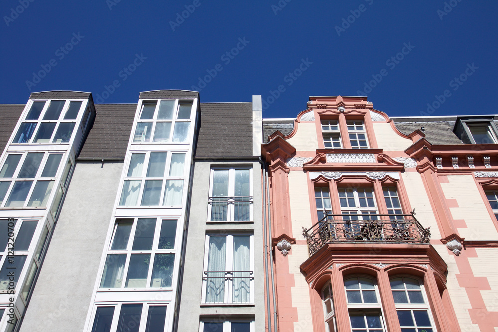 Modern next to historic architecture in Aachen, Germany with townhouses with ornate carving and dormer windows in front of a blue sky