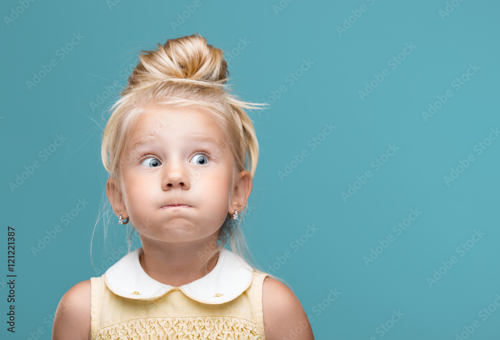 Small, young, funny girl, inflated cheeks on blue background - obrazy, fototapety, plakaty 