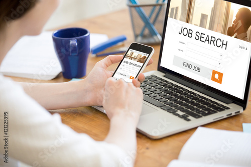 Young business woman working in office interior, searching for job online. Female looking for job using web service on smartphone. Close-up of hands holding phone. HR, recruitment, career concept photo