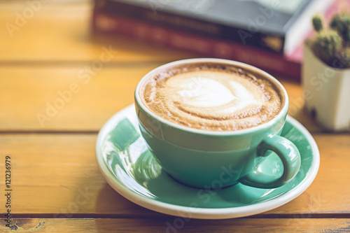 hot latte art in green cup on wooden table with book and tree.