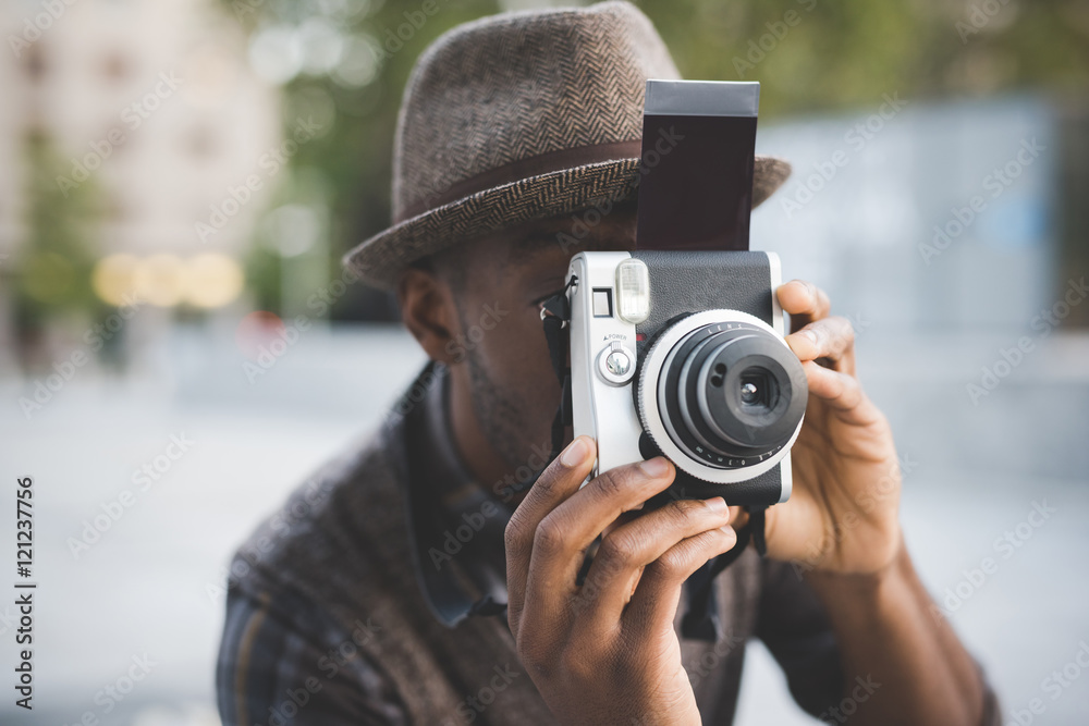 Obraz premium Half length of young beautiful afro black man outdoor in the city holding instant camera, shooting - photography, creative, artist concept