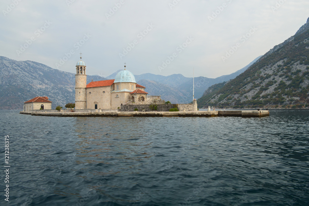 Our Lady on the Rocks islet with the Roman Catholic church of Virgin Mary in the bay of Kotor, Montenegro. Peaceful morning. Beautiful high mountains surround the bay