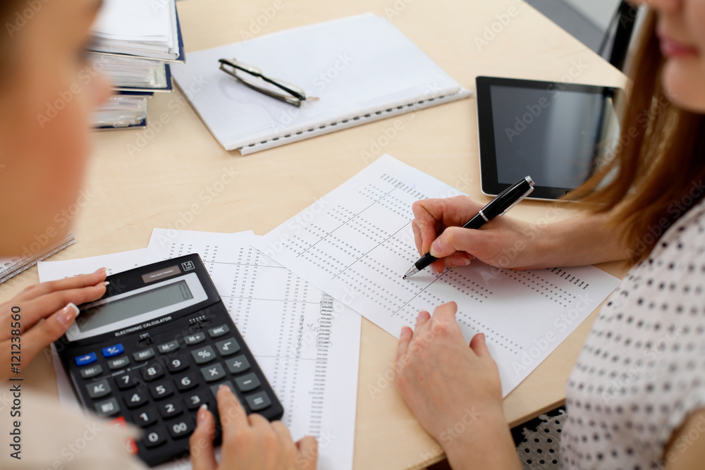 Two female accountants counting on calculator income for tax form completion hands closeup. Internal Revenue Service inspector checking financial document. Planning budget, audit concept Two female accountants counting on calculator income for tax form completion hands closeup. Internal Revenue Service inspector checking financial document. Planning budget, audit concept