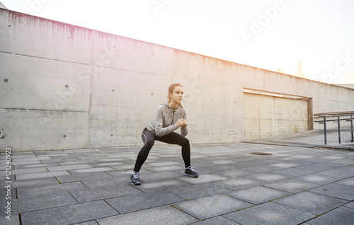happy woman doing squats and exercising outdoors