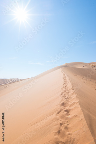 cenic ridges of sand dunes with footprints in Sossusvlei  Namib Naukluft National Park  best tourist and travel attraction in Namibia. Adventure and exploration in Africa. Backlight with sun star.