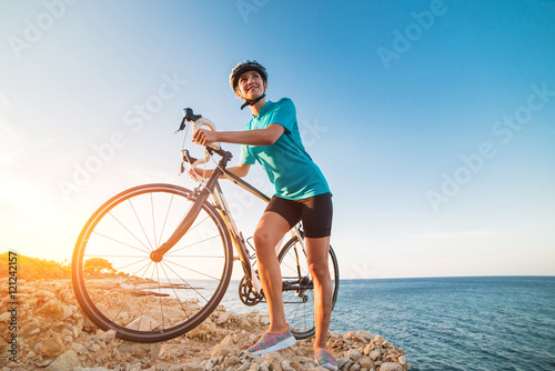 Female cyclist standing on a rock and looking at sea