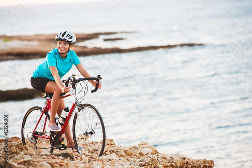 Female cyclist standing on a rock with bike and looking at sea