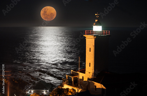 Fotografi A full moon rising over the sea with a lighthouse in the foreground