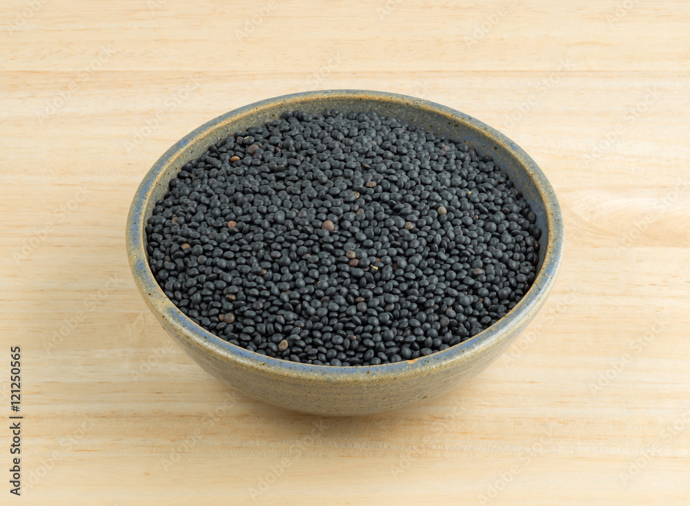 Black beluga lentils in a stoneware bowl on a wood table. Black beluga lentils in a stoneware bowl on a wood table.