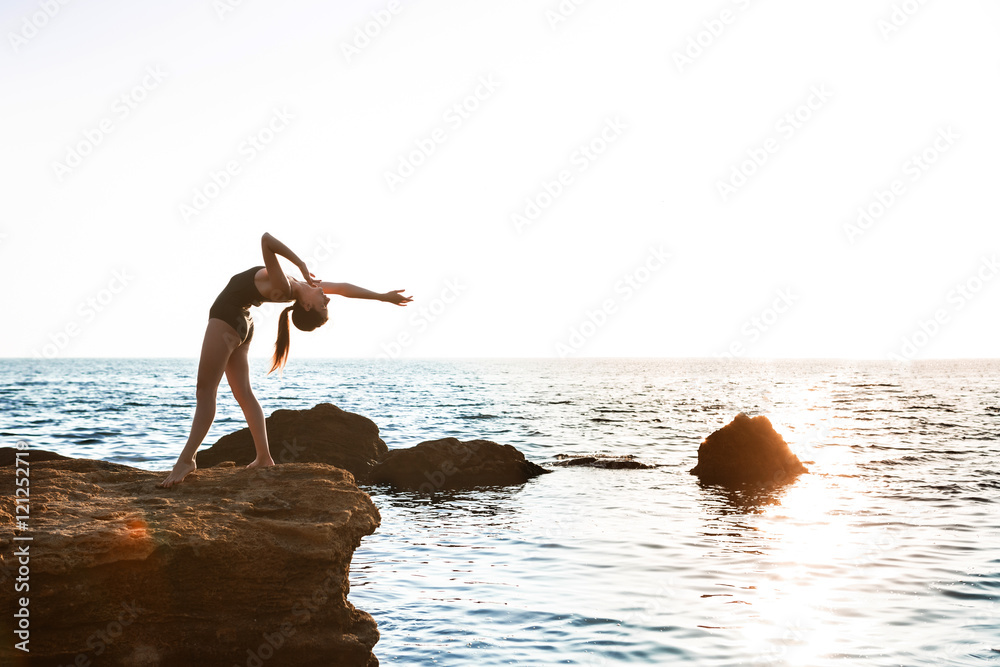 Beautiful ballerina dancing, posing on rock at beach, sea background