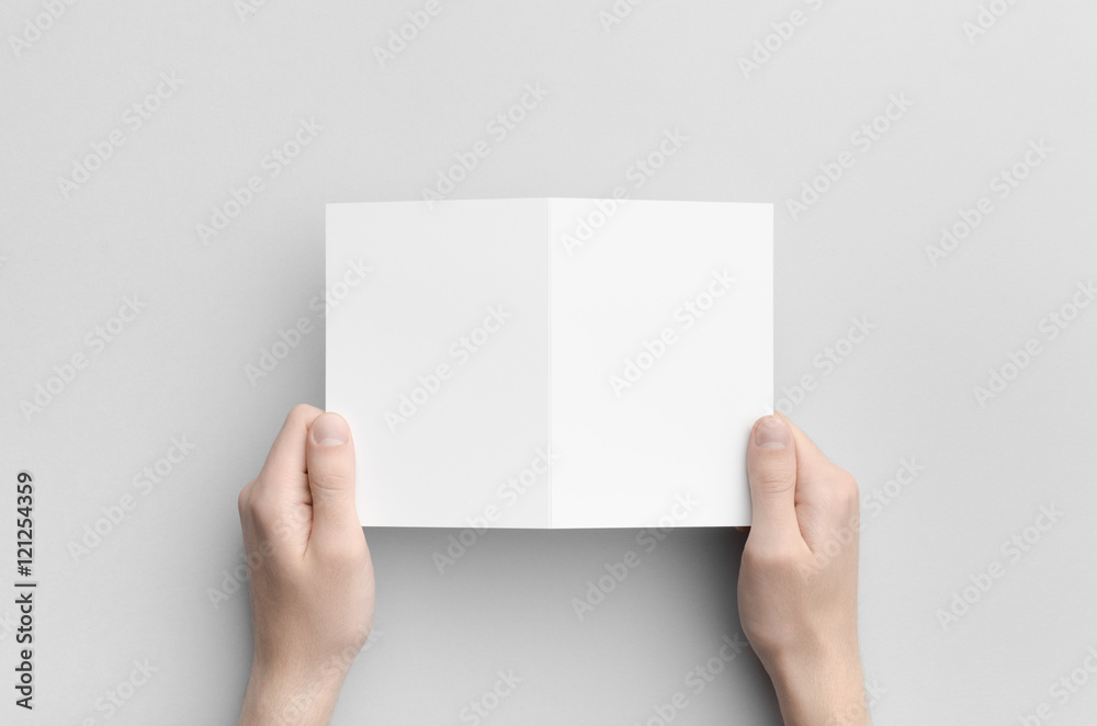 Obraz premium A6 Bi-Fold / Half-Fold Brochure Mock-Up - Male hands holding a blank bi-fold on a gray background.