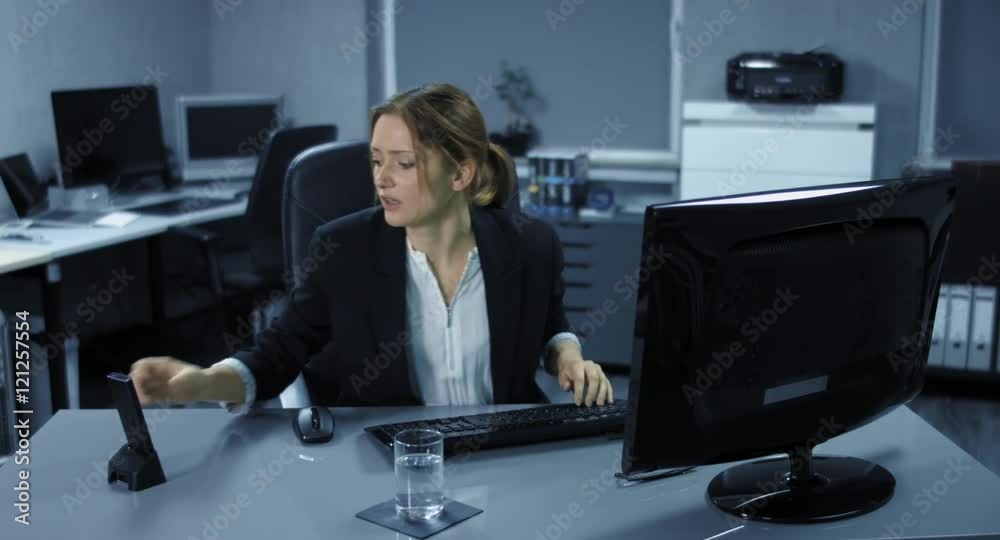 4K: Eine junge Angestellte sitzt angespannt an ihrem Arbeitsplatz. Ein Telefonat stört ihre Computerarbeit. Sie trinkt einen Schluck Wasser und ist sehr verärgert.