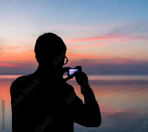 Silhouette of a man photographing the sunset on a smartphone.