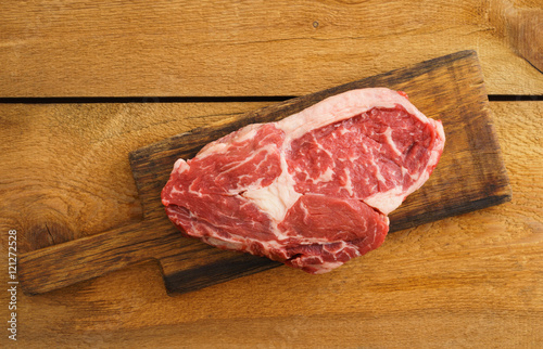 Uncooked rib eye steak on wooden board