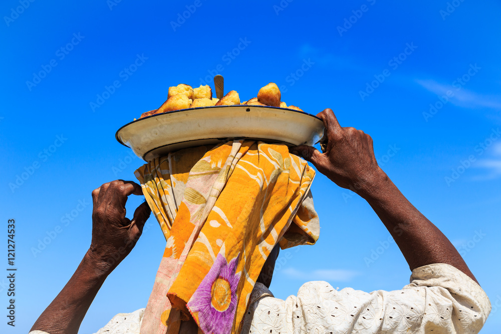 Woman carrying a dish with food on her head seen from behind - obrazy, fototapety, plakaty 