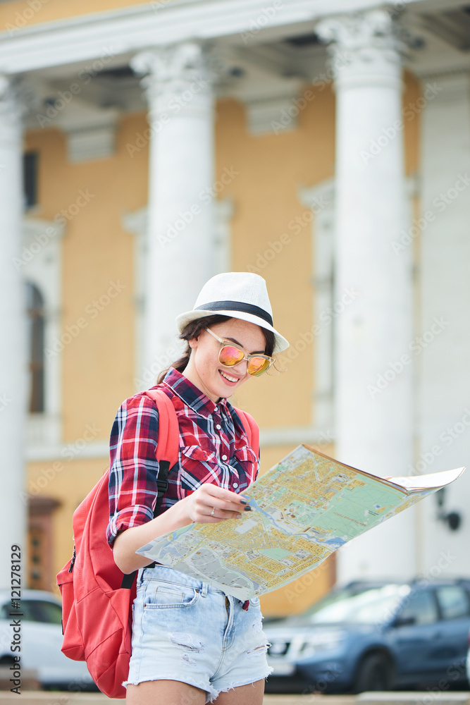 The girl tourist with hat and sunglasses holding a map and looking at her against the building with columns