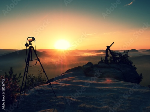Tripod with running camera on  peak ready for photography. Sharp rocky peaks