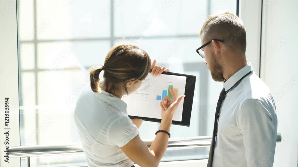 colleagues discussing graphs in office near window colleagues discussing graphs in office near window