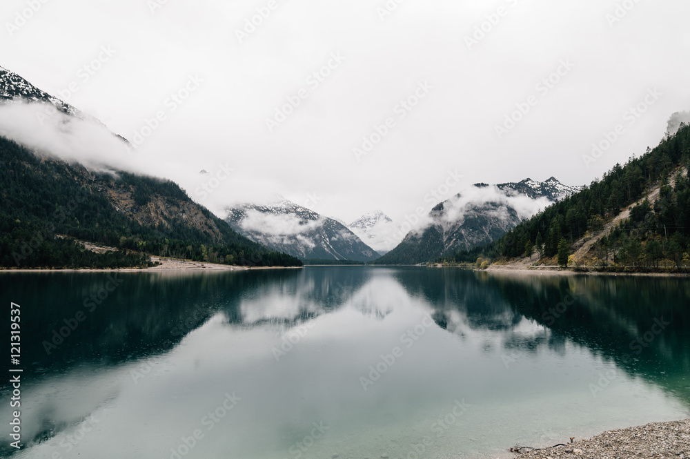 Mountain lake and  water reflections. Plansee lake located in Austria a cloudy and foggy day. Horizontal composition, space for copy