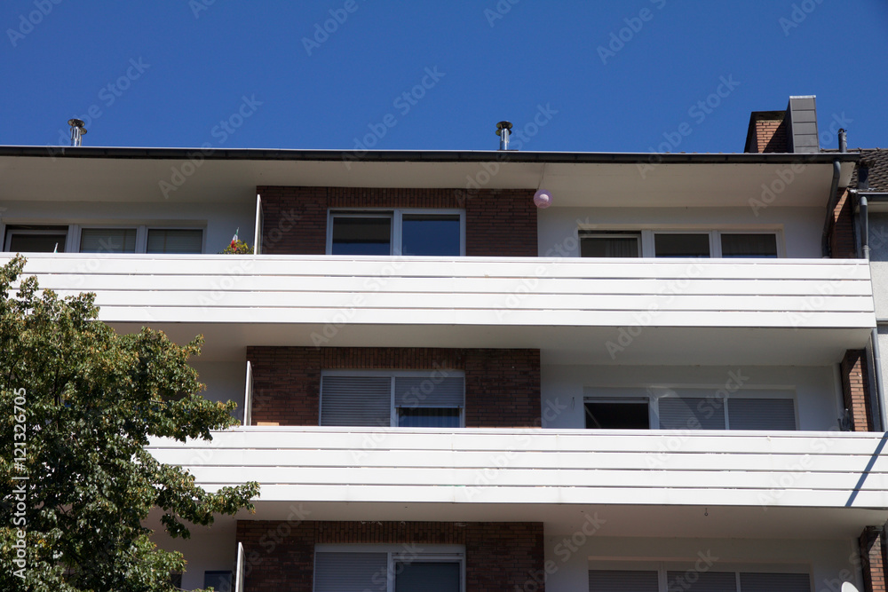 Residential apartment or hotel exterior from street level view. Tree in foreground with blue sky background Residential apartment or hotel exterior from street level view. Tree in foreground with blue sky background