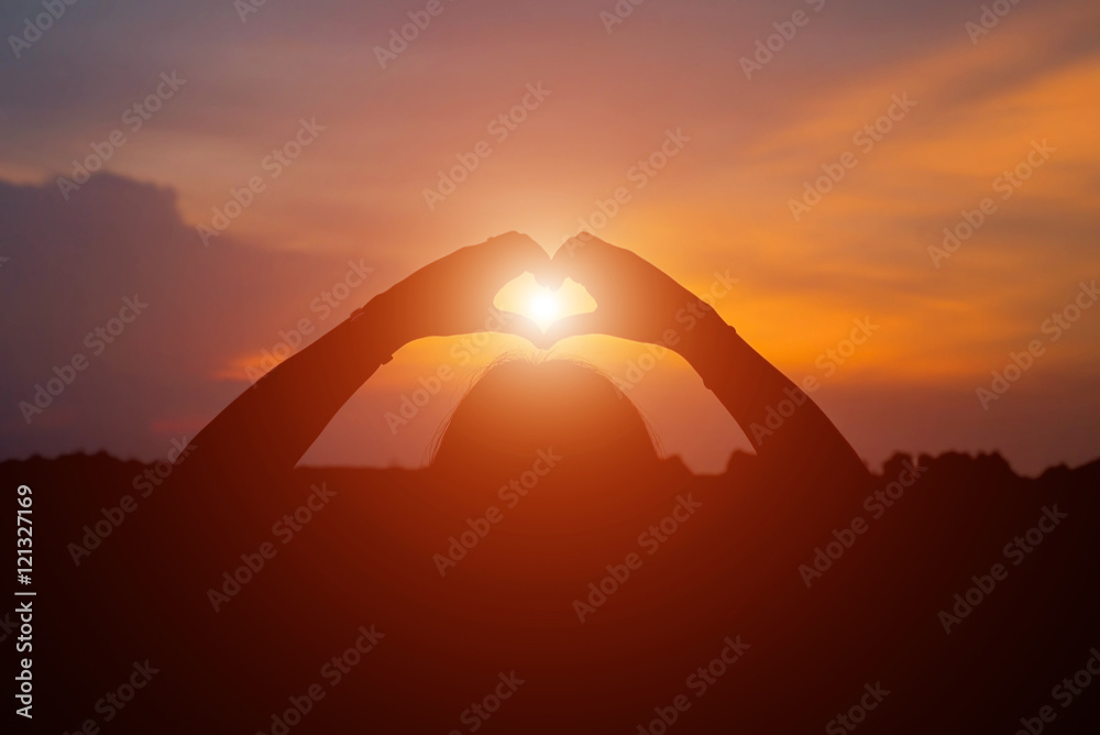silhouette of woman heart shape making of hands against at sunse