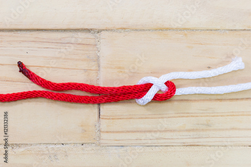 sheet bend knot made with red rope on wooden background.