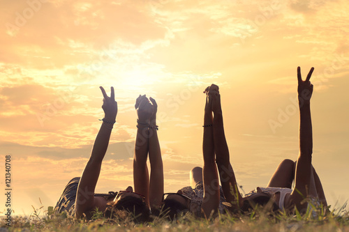 Fotografie young women lying in the meadow raise their arms in a sign of friendship
