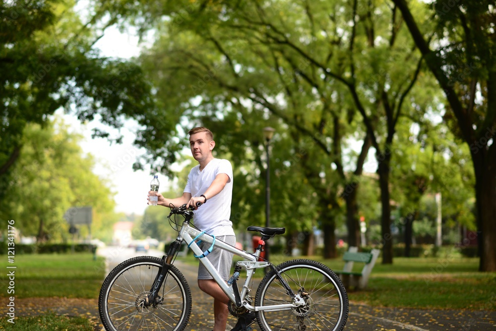 Young blond man on bicycle stoping to drink water Young blond man on bicycle stoping to drink water