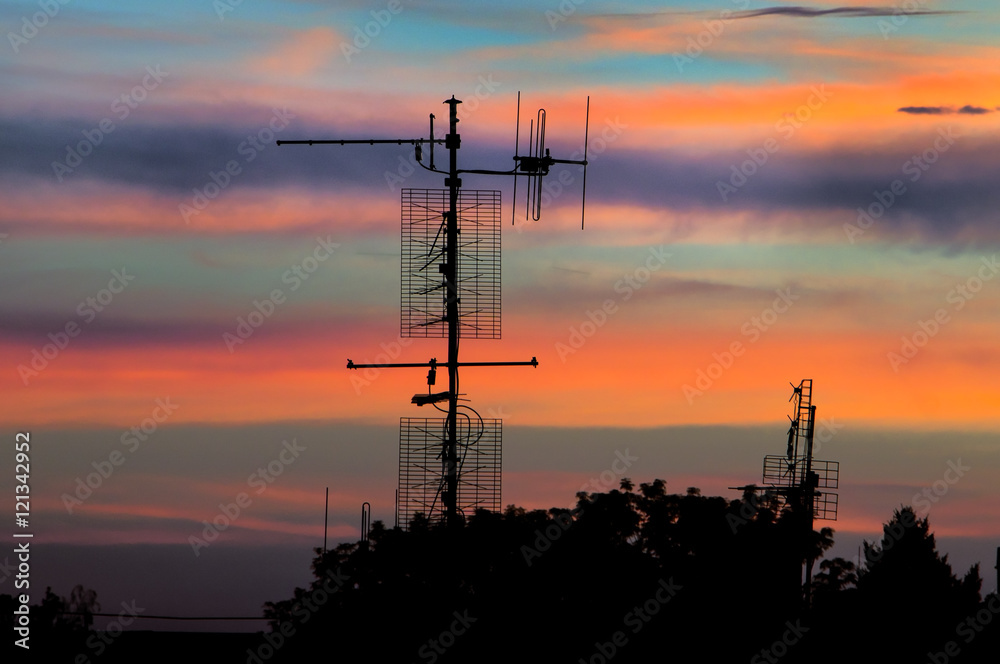 silhouette of televisions antennas with sunset cloudy sky background