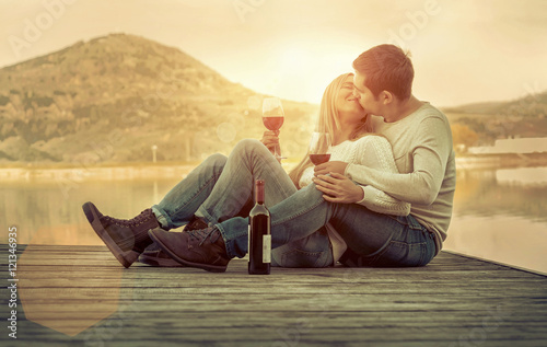 Romantic Couple sitting on the pier with red wine.