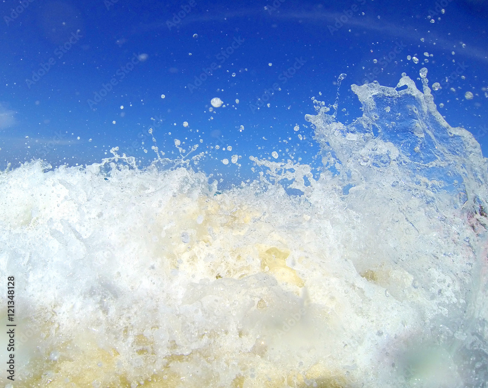 Close up of moving wave with splashing white bubble over the sand with blue sky