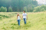 A lovely couple walking in a forest area, green grass all around them, holding hands,looking smiling at each other