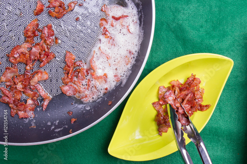 Chef poring fried bacon from pan with tongs photo