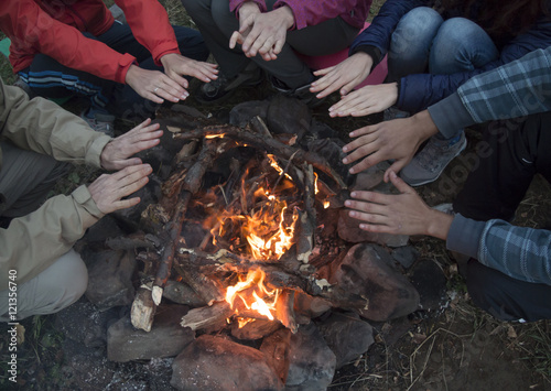 young men and women hands warm by the fire. They sit around the