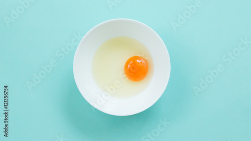 Top view of raw egg in white bowl on blue background.