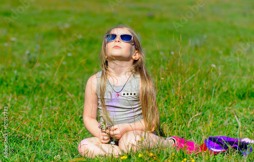caucasian little blonde girl sitting on green field in forest