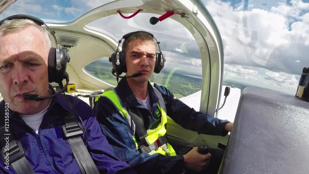 Time lapse with cockpit view of young student pilot in safety vest aviating airplane with middle aged flight instructor sitting beside and mentoring him